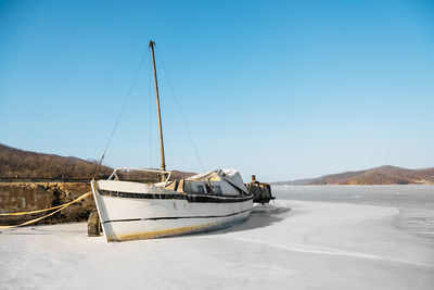 Old wooden sailboat moored at pier and frozen in sea ice against backdrop of amazing sea winter 