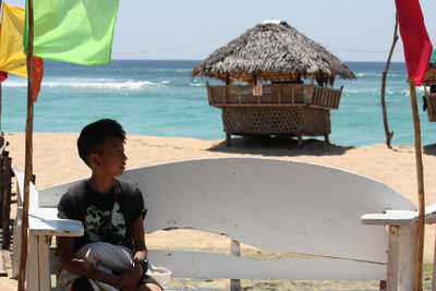 Boy sitting on beach against sky