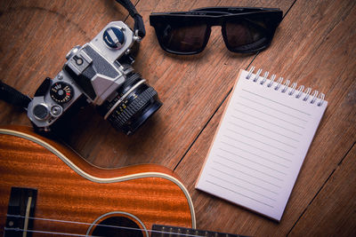 High angle view of guitar with camera and note pad on wooden table