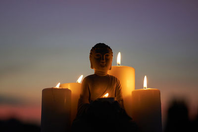 Close-up of man with illuminated candle against sky during sunset
