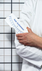 Midsection of man holding paper while standing against white wall