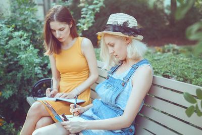 Friends writing n diaries while sitting on bench at park