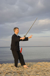 Full length of man practicing tai chi at beach against cloudy sky