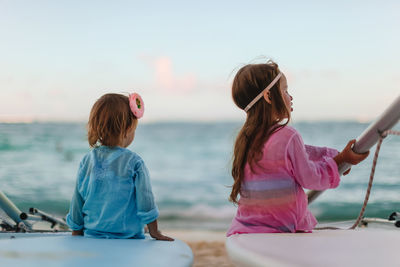 Rear view of women sitting on sea shore against sky