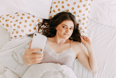 Beautiful girl talking on the phone using technology while lying in bed at home