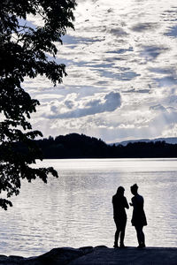 Silhouette couple standing by lake against sky