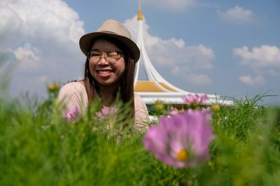 Young woman with pink flower in field against sky