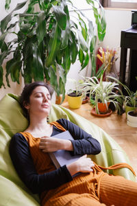 Woman sitting on potted plant at home