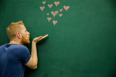 Young man gesturing with heart shapes on blackboard