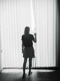 Rear view of woman standing against curtain at home