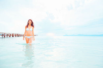 Portrait of young woman in bikini standing on beach