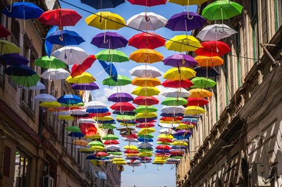 Low angle view of multi colored umbrellas hanging against buildings