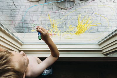 Overhead view of shirtless boy writing on window at home