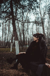 Woman standing by tree trunk in forest