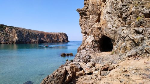 Rock formations by sea against clear blue sky