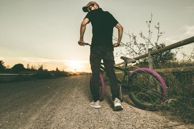 Rear view of man standing by bicycle against sky during sunset