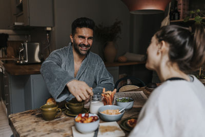 Happy man enjoying breakfast with non-binary person at home