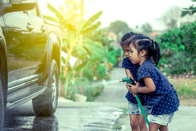 Side view of twin sisters cleaning car