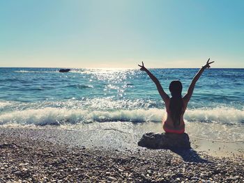 Rear view of man with arms raised at beach against sky