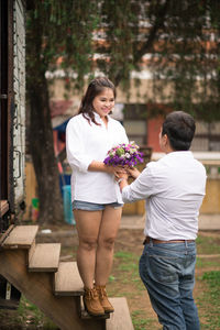 Man giving bouquet to girlfriend while standing on field