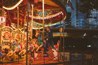 Boy sitting on illuminated carousel in amusement park