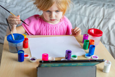 Little girl painting with paints, looking at tablet, sitting at the table. online school concept.