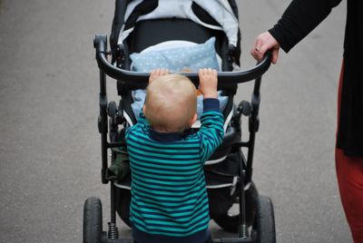 Cropped image of person walking with boy pushing baby stroller on footpath