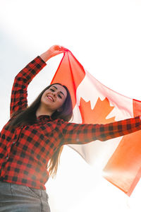 Young millennial brunette woman holding the national flag of canada. canadian flag or the maple leaf