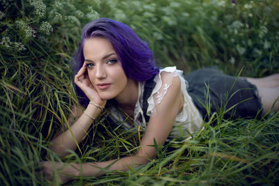 Portrait of a teenage girl with purple hair and an earring in her nose lying in the grass in nature