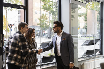 Happy couple shaking hand with real estate agent at entrance of office