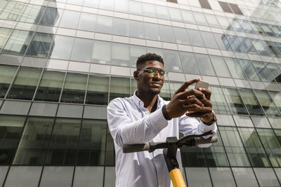 Young man using smart phone in front of glass building