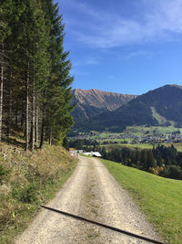 Empty road amidst trees and mountains against sky