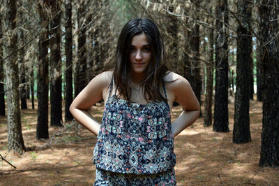 Portrait of young woman standing amidst trees at forest