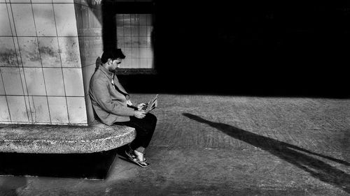 Side view of man reading newspaper while sitting on seat