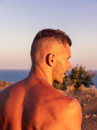 Portrait of shirtless man looking away against sky