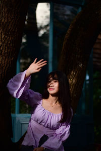 Portrait of young woman standing by tree trunk