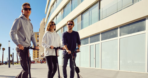 Friends using push scooters in city on sunny day
