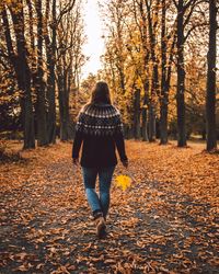 Rear view of woman walking amidst trees during autumn