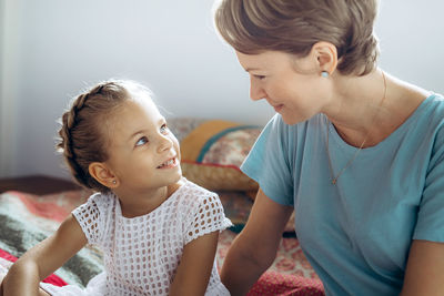 Close-up of mother talking with daughter sitting on bed at home