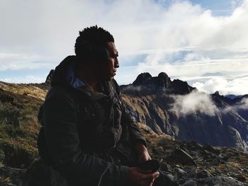 Man listening music on mountain against sky