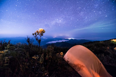 Tent at mountain peak against blue sky at night
