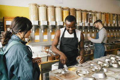 Smiling male owner talking with customer while working in food store