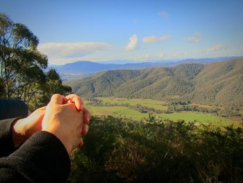 Midsection of person relaxing on mountain against sky