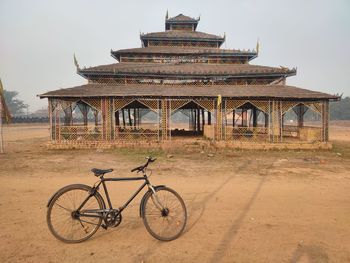 Bicycle leaning against building on field against sky