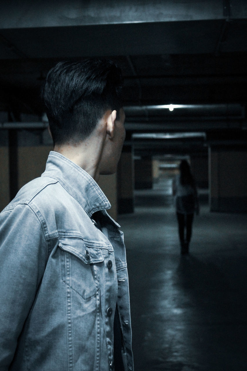 rear view, real people, men, lifestyles, casual clothing, architecture, focus on foreground, built structure, standing, indoors, leisure activity, city, adult, clothing, walking, waist up, illuminated, jeans