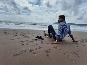 Full length of man sitting on shore at beach against sky