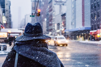 Rear view of person in hat walking in city during snowfall