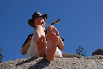 Woman playing ukulele sitting on rock at magnetic island against clear sky