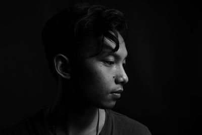 Portrait of young man looking away against black background