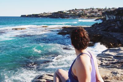 Woman sitting at shore against sea